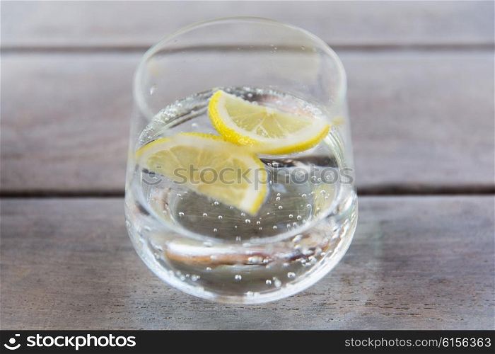 drink and refreshment concept - glass of sparkling water with lemon slices on table. glass of sparkling water with lemon on table