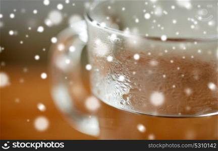 drink concept - close up of glass with hot water over snow. close up of glass with hot water