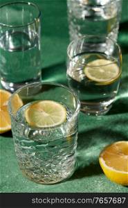 drink, detox and diet concept - close up of glasses with water and lemons on emerald green background. glasses with water and lemons on green background