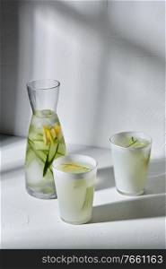 drink, detox and diet concept - glasses with fruit water or lemonade with lemon and cucumber dropping shadows on white surface. glasses with lemon water and cucumber on table