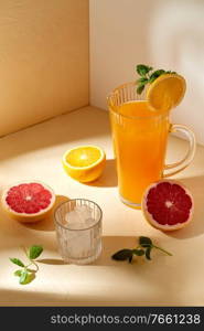 drink, detox and diet concept - jug with orange juice, cut grapefruit and ice cubes in glass on table. orange juice, grapefruit and ice in glass on table