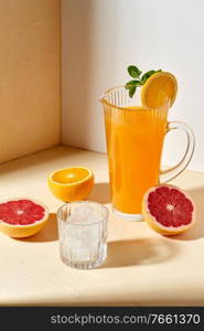 drink, detox and diet concept - jug with orange juice, cut grapefruit and ice cubes in glass on table. orange juice, grapefruit and ice in glass on table