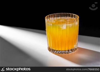 drink, detox and vitaminic concept - glass of orange juice or lemonade with ice on table. glass of orange juice with ice on table