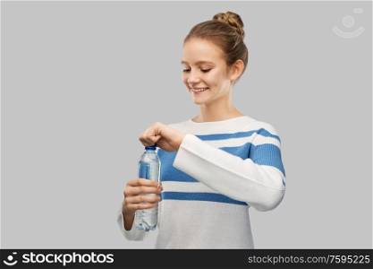 drink, health and people concept - happy smiling teenage girl in pullover opening bottle of water over grey background. smiling teenage girl opening bottle of water
