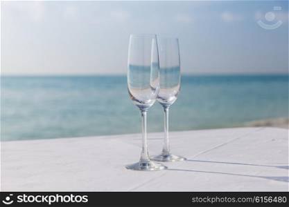 drink, holidays, summer vacation and celebration concept - close up of two champagne glasses on table over sea on beach