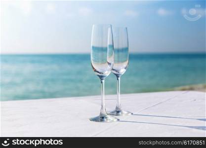drink, holidays, summer vacation and celebration concept - close up of two champagne glasses on table over sea on beach