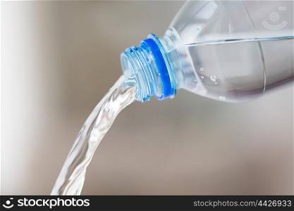 drinking, healthy eating and food storage concept - close up of water pouring from plastic bottle