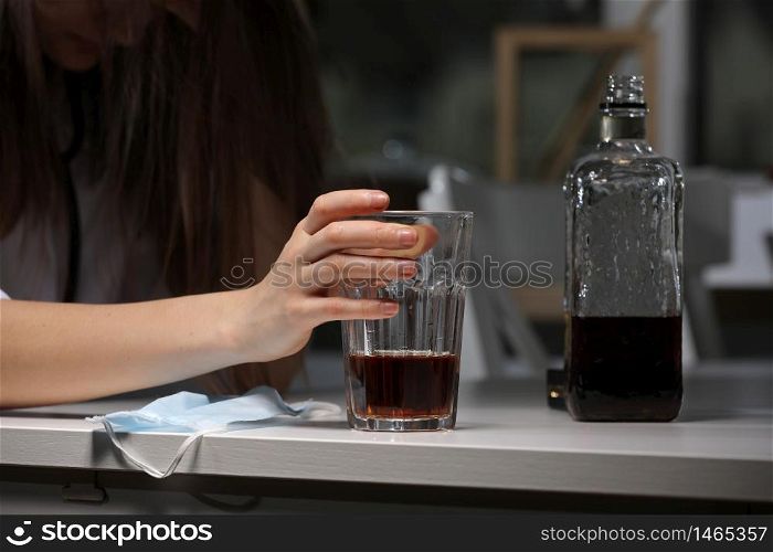 Drinking problem alcoholism during coronavirus isolation quarantine time concept. woman is holding glass with alcohol drink. face mask on background. Drinking problem alcoholism during coronavirus isolation quarantine time concept. Hand holding glass with alcohol drink. face mask on background.