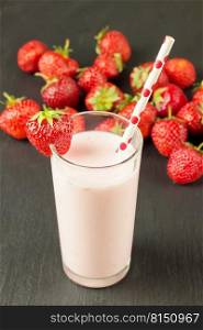 Drinking strawberry yogurt in the glass with a straw on a black slate board. Strawberry yogurt in the glass on blakc slate background