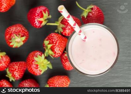 Drinking strawberry yogurt in the glass with a straw on a black slate board. Flat lay, top view. Strawberry yogurt in the glass on black slate background