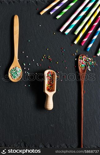Drinking straws and sugar sprinkle dots on slate background