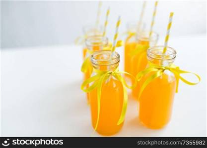 drinks and party concept - close up of orange juice or lemonade in decorated glass bottles with paper straws. orange juice in glass bottles with paper straws