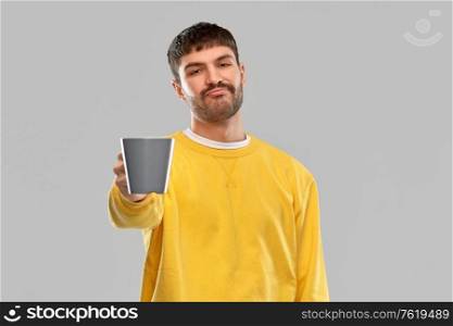 drinks and people concept - displeased young man with coffee cup over grey background. displeased young man with coffee cup