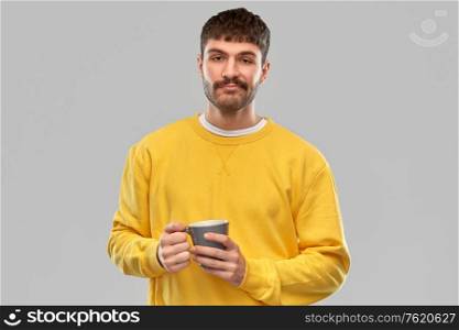 drinks and people concept - displeased young man with coffee cup over grey background. displeased young man with coffee cup
