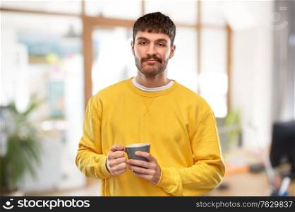 drinks and people concept - displeased young man with coffee cup over office background. displeased young man with coffee cup at office