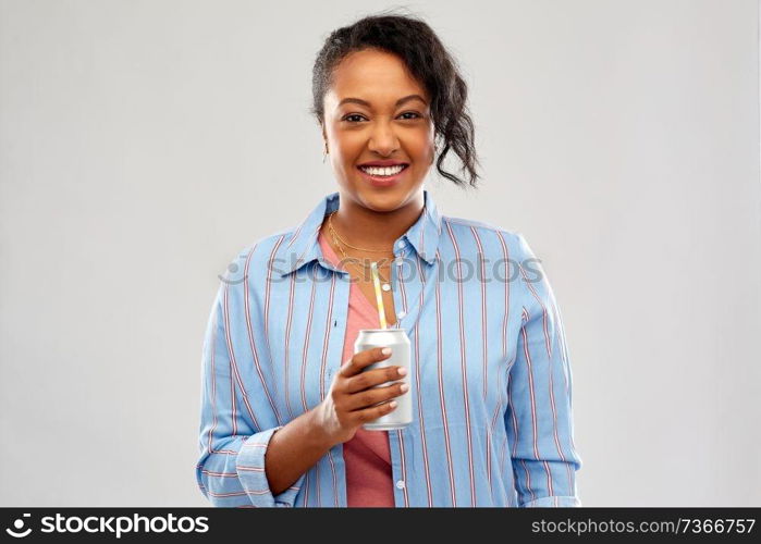 drinks and people concept - happy african american young woman drinking soda from can with paper straw over grey background. happy african american woman with can drink