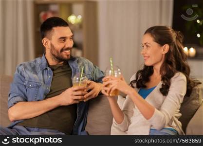 drinks and people concept - happy couple drinking takeaway juice from plastic cups with paper straws at home in evening. happy couple drinking takeaway juice at home