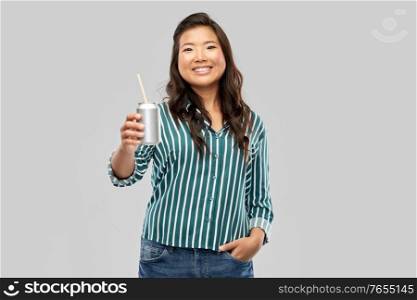 drinks and people concept - happy smiling young asian woman drinking soda from can with paper straw over grey background. happy smiling asian woman with can drink