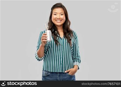 drinks and people concept - happy smiling young asian woman drinking soda from can with paper straw over grey background. happy smiling asian woman with can drink