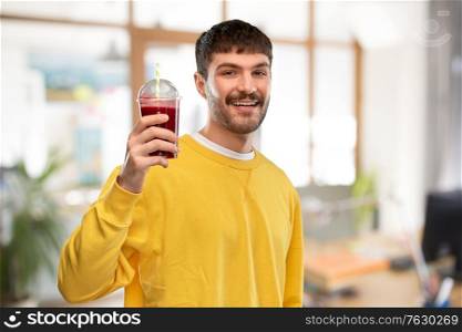 drinks and people concept - happy smiling young man holding tomato juice in takeaway plastic cup with paper straw over office background. happy man with juice in plastic cup at office