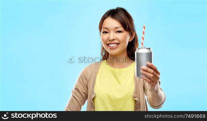 drinks and people concept - happy young asian woman drinking soda from can with paper straw over blue background. happy asian woman holding can drink with straw