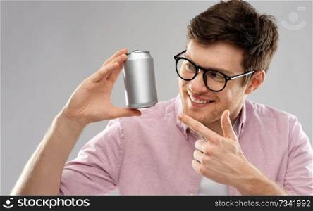 drinks and people concept - happy young man in glasses holding tin can with soda over grey background. happy young man holding tin can with soda