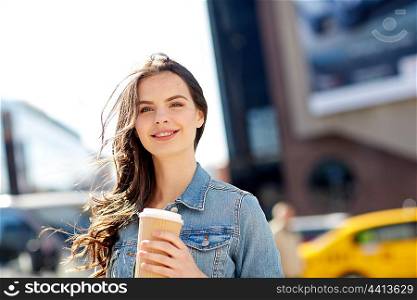 drinks and people concept - happy young woman or teenage girl drinking coffee from paper cup on city street. happy young woman drinking coffee on city street