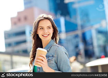 drinks and people concept - happy young woman or teenage girl drinking coffee from paper cup on city street. happy young woman drinking coffee on city street