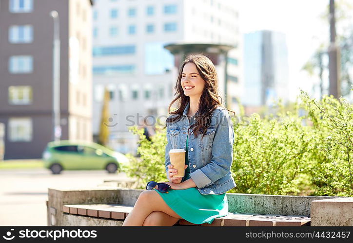 drinks and people concept - happy young woman or teenage girl drinking coffee from paper cup sitting on on city street bench. happy young woman drinking coffee on city street