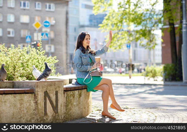 drinks and people concept - happy young woman or teenage girl drinking coffee from paper cup sitting on on city street bench. happy young woman drinking coffee on city street