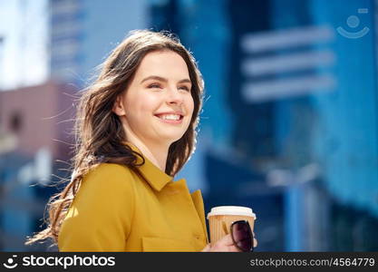 drinks and people concept - happy young woman or teenage girl drinking coffee from paper cup on city street. happy young woman drinking coffee on city street