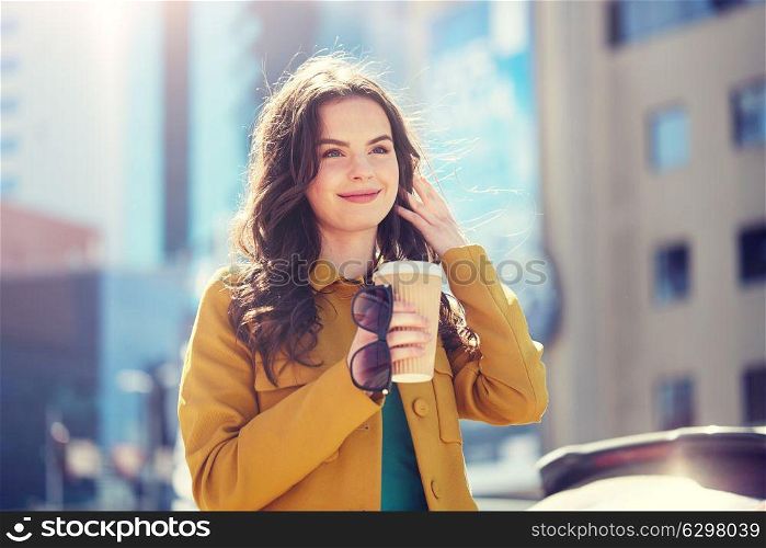 drinks and people concept - happy young woman or teenage girl drinking coffee from paper cup on city street. happy young woman drinking coffee on city street. happy young woman drinking coffee on city street