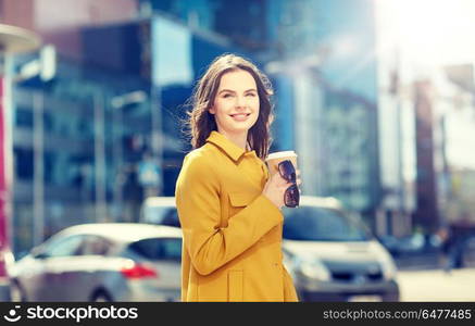 drinks and people concept - happy young woman or teenage girl drinking coffee from paper cup on city street. happy young woman drinking coffee on city street. happy young woman drinking coffee on city street