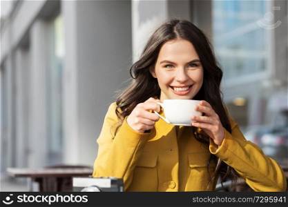 drinks and people concept - happy young woman or teenage girl drinking hot chocolate at city street cafe terrace. teenage girl drinking hot chocolate at city cafe