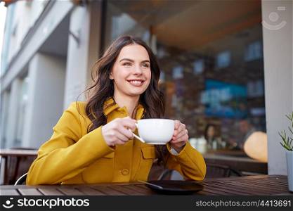 drinks and people concept - happy young woman or teenage girl with cup drinking cocoa at city street cafe terrace. happy woman drinking cocoa at city street cafe