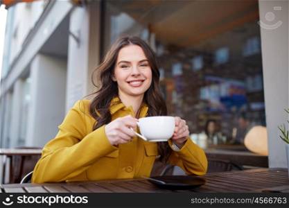 drinks and people concept - happy young woman or teenage girl with cup drinking cocoa at city street cafe terrace. happy woman drinking cocoa at city street cafe