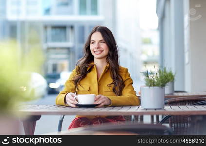 drinks and people concept - happy young woman or teenage girl with cup drinking cocoa at city street cafe terrace. happy woman drinking cocoa at city street cafe