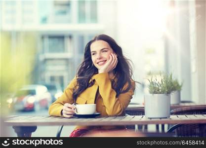 drinks and people concept - happy young woman or teenage girl with cup drinking cocoa at city street cafe terrace and dreaming. happy woman drinking cocoa at city street cafe