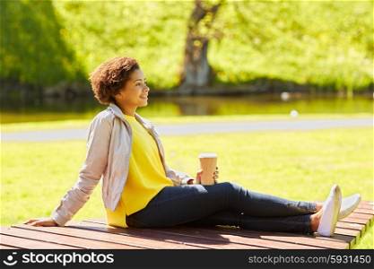drinks and people concept - smiling african american young woman or teenage girl drinking coffee from paper cup at summer park . happy african woman drinks coffee at summer park