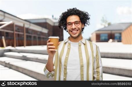 drinks and people concept - smiling young man in glasses with takeaway coffee cup over city street background. smiling young man with takeaway coffee cup in city