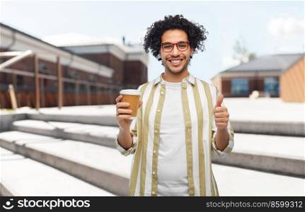 drinks and people concept - smiling young man in glasses with takeaway coffee cup showing thumbs up gesture over city street background. man with coffee cup showing thumbs up in city