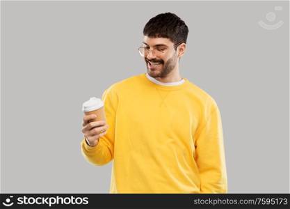 drinks and people concept - smiling young man with takeaway coffee cup over grey background. smiling young man with takeaway coffee cup