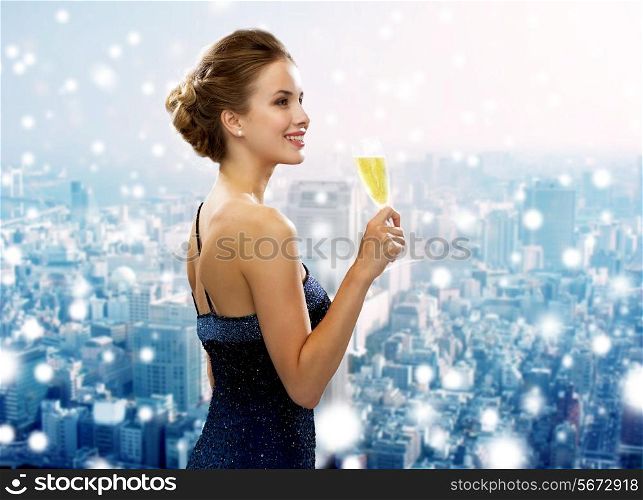 drinks, christmas, holidays and people concept - smiling woman in evening dress with glass of sparkling wine over snowy city background