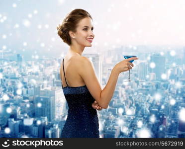 drinks, christmas, holidays and people concept - smiling woman in evening dress holding cocktail over snowy city background