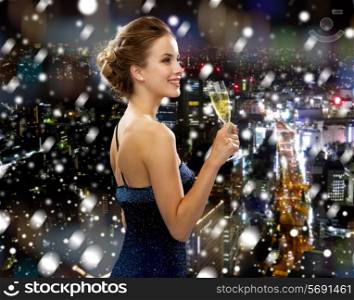 drinks, christmas, holidays and people concept - smiling woman in evening dress with glass of sparkling wine over snowy night city background