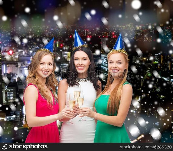 drinks, christmas, winter holidays, people and celebration concept - smiling women in party hats with glasses of sparkling wine over snowy night city background