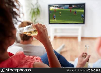 drinks, entertainment and people concept - close up of woman drinking non-alcoholic beer from bottle and watching soccer or foortball game on tv at home with friends. friends drinking beer and watching soccer on tv