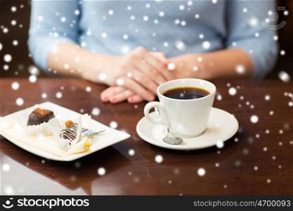drinks, food, people, christmas and winter concept - close up of woman hands with coffee cup and dessert over snow