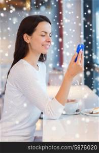 drinks, food, people, technology and lifestyle concept - smiling young woman with smartphone drinking coffee at cafe over snow effect