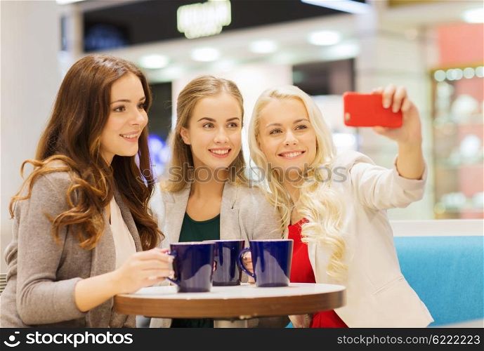 drinks, friendship, technology and people concept - happy young women with cups sitting at table and taking selfie with smartphone in cafe